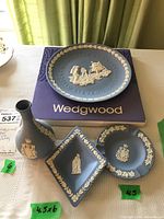 Full set of Wedgwood items on table displaying commemorative plate on original box, vase, ashtray and tray with green price tags.