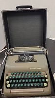 Smith Corona typewriter in olive green with round green keys shown inside the case.