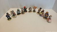 Wide angled photo showing all 11 Beatrix Potter character figurines arranged in a semi-circle on a white surface against a beige background.