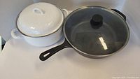 Photo of the deep cast iron pan with its glass lid and the white pot with lid together.