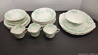 Full view of stacked plates, cups, and saucers showing the green floral design and gold trim on white china