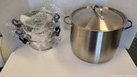 Large stainless steel stock pot with lid and bundled two-tier steamer set on white background.