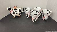 Full lot view showing cow-shaped teapot and 4 matching cow motif mugs