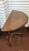 Half moon shaped wood accent table closed, showing the top surface with a light water stain and carved legs