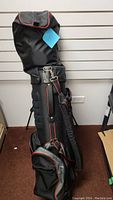 Full view of the black golf bag with red trim standing upright, showing compartments and attached strap.