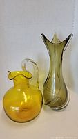 Yellow glass pitcher and tall green vase shown together.