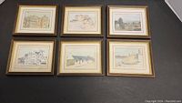 Six small framed Neil Macleod prints arranged on a black surface, showing varied scenes including buildings, bridge, and a landscape.