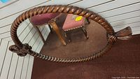 Full view of the oval mirror showing twisted rope carved wood frame and part of a red upholstered chair in background.