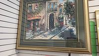 Framed painting showing an urban street view with café tables and architectural details.
