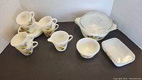 Full set layout showing four teacups, creamer, sugar bowl, small bowl, butter dish with lid, casserole dish with lid all decorated with autumn floral design in yellow and orange on white glass.