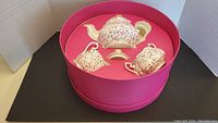 Top-down view of teapot, creamer, and sugar bowl nested in original pink presentation box.