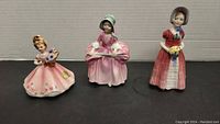 Front view of the three figurines showing details of the dresses and bonnets.