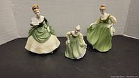 Front view of three Royal Doulton female figurines in green and cream period dresses, arranged left to right.