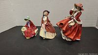 Three Royal Doulton porcelain figurines from front view including 'Linda', 'Paisley Shawl', and 'Top o' the Hill'.
