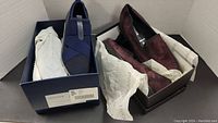Two pairs of ladies slip on shoes in their respective boxes with tissue paper inside and outside the boxes.