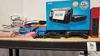Shelf view showing Wii U box, red Wii console, game cases, controllers and cords