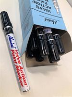 Photo showing multiple black Markal Valve Action paint markers inside an open blue box.