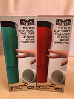 Two boxed MightyMug travel mugs side by side, one teal and one red, showing front packaging with product name and image