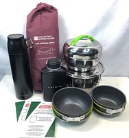 Full view of lot contents showing cookware set, flask, mini cup, self-inflating pillow in bag, and mantle packages.