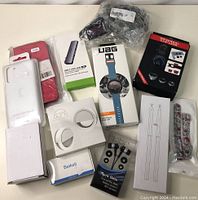 Lot of new assorted electronics accessories displayed on table, multiple items in original and sealed packaging visible.