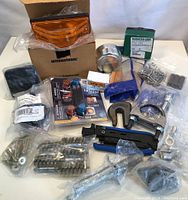 A wide view of the lot showing an amber vehicle light lens in International branded packaging, various metal fasteners, clamps, crimping tool, and some blue and silver hardware components packed in plastic bags.