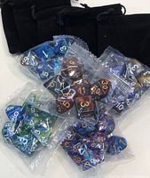 Photo showing 35 new assorted polyhedral dice in blue, brown, green, purple colors packaged loosely with multiple black velvet drawstring bags