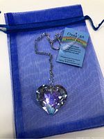 Heart-shaped crystal prism suncatcher with chain, keyring, and tag on blue sheer pouch.