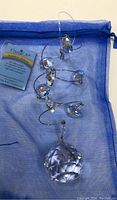 Full view of the Crystal Art suncatcher with faceted crystals, spiral wire, and product tag, laid on blue drawstring bag.