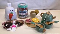 Photo showing white bunny night light holding carrot, jar of Unicorn Sparkle slime, pink glitter kids sunglasses, and wooden toy tea set parts including teapot, cups, spoons, pitcher and flower-shaped tray.