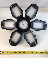 Top view of the LED socket light with six foldable LED panels arranged in a flower shape around a central circular hub. Measuring tape shows size approximately 11 inches in diameter.