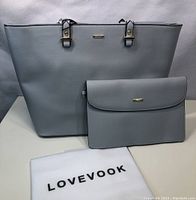 Two grey handbags, a large purse and a smaller clutch, with white dust bag labeled 'LOVEVOOK'