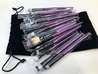 Photo of 20 Meloision makeup brushes with purple handles, still individually wrapped, displayed on and alongside a black drawstring pouch.