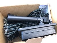 Box containing bundled dark green wire LED solar string lights with ground stake and solar panel visible