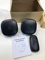 Two black receiver units, one black push button transmitter, and user manual for wireless doorbell model MS2021S1 on white background.