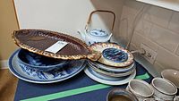 Display of an assortment of Asian style ceramics including a large brown fish-shaped platter, blue and white plates and bowls, and a white and blue teapot on a kitchen counter