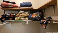 Shelf of assorted folded blankets and comforters including woven, crocheted, and floral patterns