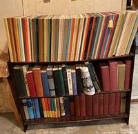 Two-tier bookshelf showing top shelf loaded with thin clothbound Horizon volumes in multiple colors and bottom shelf with assorted hardcover and clothbound books including red cloth Gibbon set