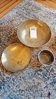Three brass items - large engraved bowl, medium engraved bowl, small plain cup on carpeted floor