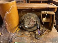 Vintage Calculagraph clock with metal housing and accessories arranged on wooden table including a string spool holder, small jar with scissors, pens, and wooden template piece.