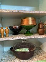 Shelf with the cast iron casserole with glass lid labeled 'Cast Iron'. Surrounding items include salt and pepper shakers, copper jug, and two glass bowls.