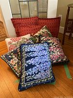 Group shot of all eight cushions showing three red lattice-patterned and five floral needlepoint cushions