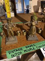 Two brass Dutch figurines, male and female, each carrying swinging water jugs, with measuring tape showing size around 5 inches tall.