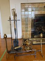 Full set including brass teapot on warmer stand, andirons, fireplace tooling stand with tools, and candle snuffer arranged near fireplace.