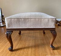 Front view of the footstool showing carved wooden legs and upholstered cushion.