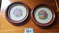 Front view of two round framed petit point floral embroideries on wooden frames with gold trim, showing size reference and frame wear.