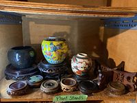 Overview of wooden plant stands and three ceramic ginger pots displayed on and around the stands in a wooden shelf.