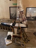 Remote control sailboat on wooden stand with fabric sails and two framed black and white sailboat pictures behind