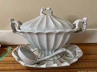 Full view of the tureen with lid on the underplate alongside the ladle placed on the underplate to show all items included in the lot.