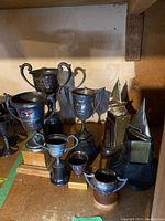 Eight silver-tone sailing trophies of various sizes and shapes, with some mounted on wooden bases, some shaped like sailboats.