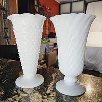 Two vintage milk glass vases photographed upright on a granite surface, showing hobnail and swirl textures clearly with scalloped edges at the rims.